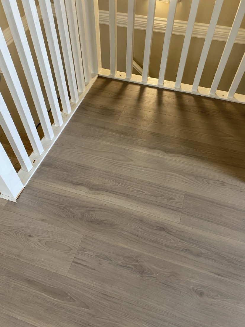 Stair landing with a grey-brown plank floor and white railings, installed by Hearth & Plank